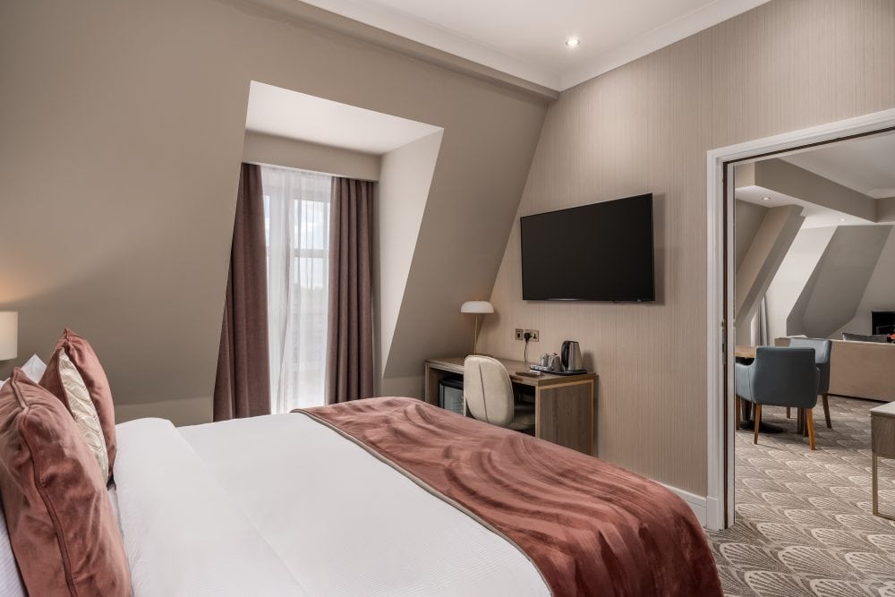 Professional hotel photography of a hotel suite with the bedroom in the foreground and living space through a doorway